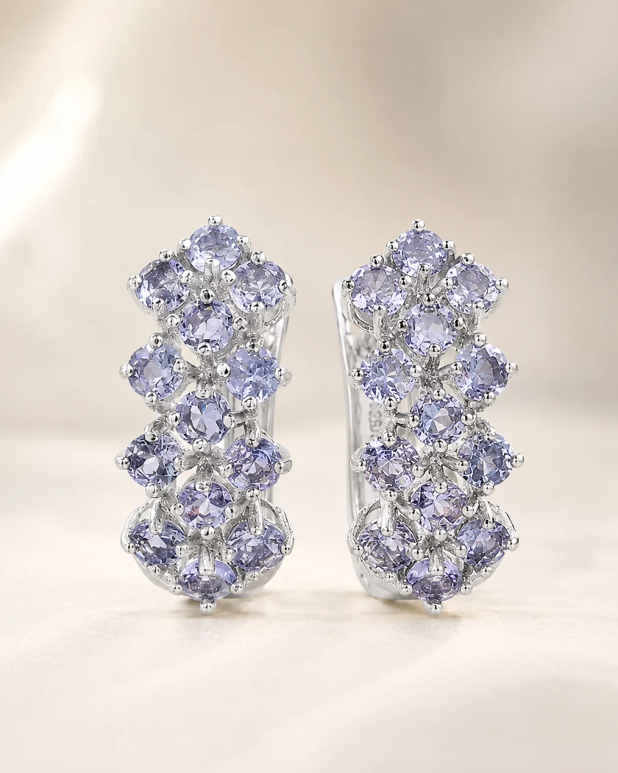 A pair of silver clip earrings set with rows of small round lavender tanzanites, standing upright on a cream surface.