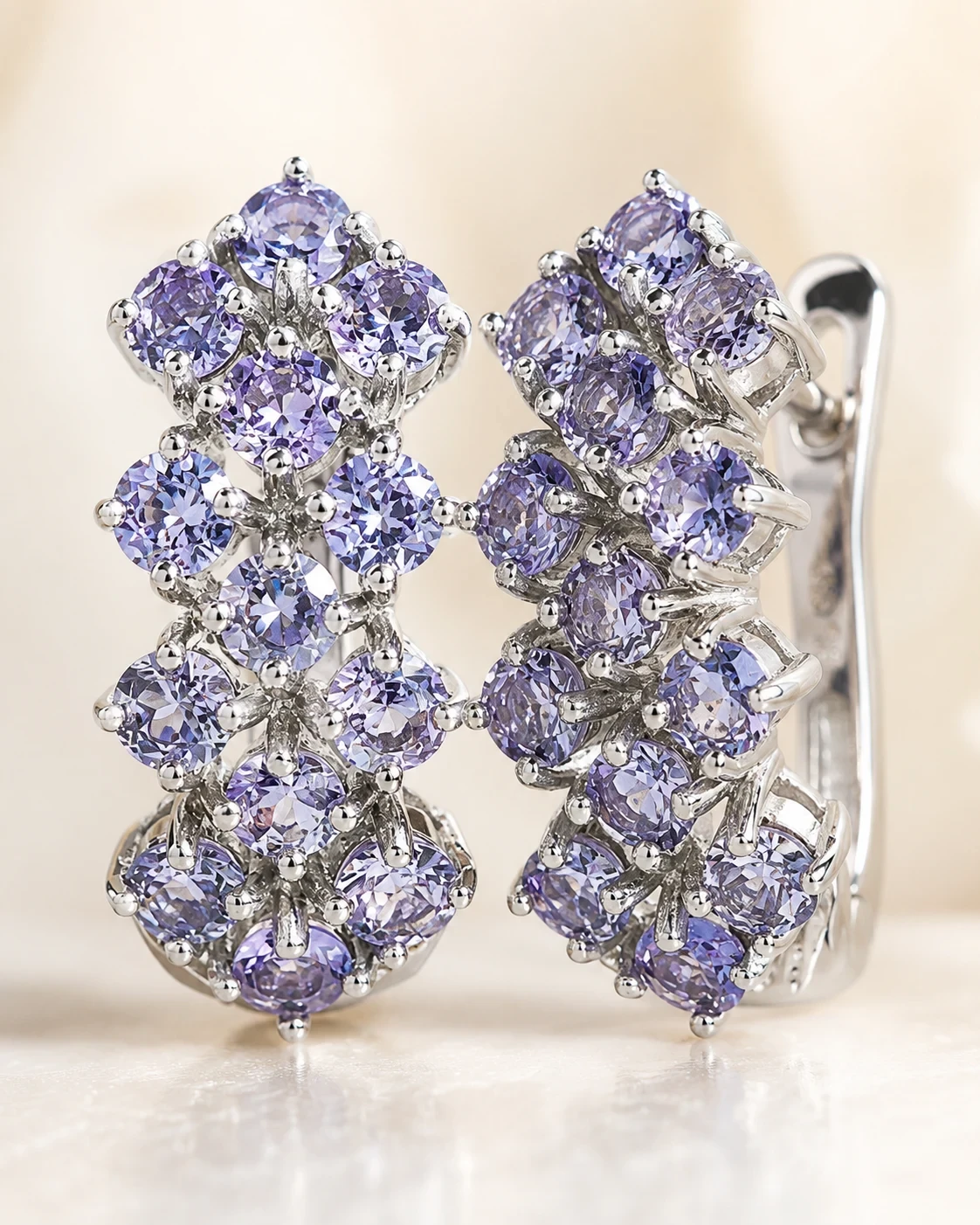 The earrings on a pale stone plinth, lit from the side so the stones read violet against the silver.