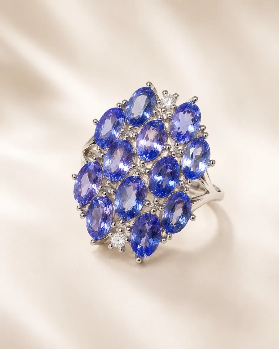 A silver ring set with twelve oval violet-blue tanzanites in a marquise-shaped cluster, on cream silk.