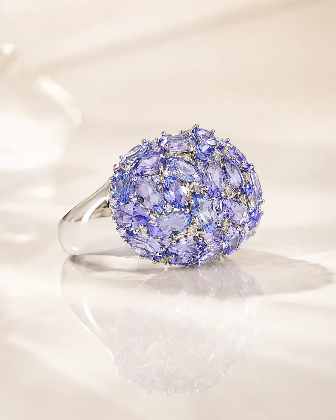 A domed silver ring paved with oval violet-blue tanzanites and small white stones, resting on cream silk.